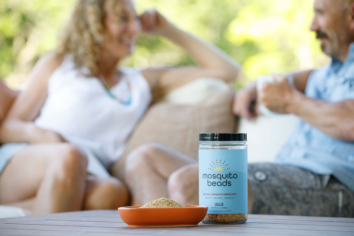 Mosquito beads container on a table with a blurred background of two people sitting outdoors.